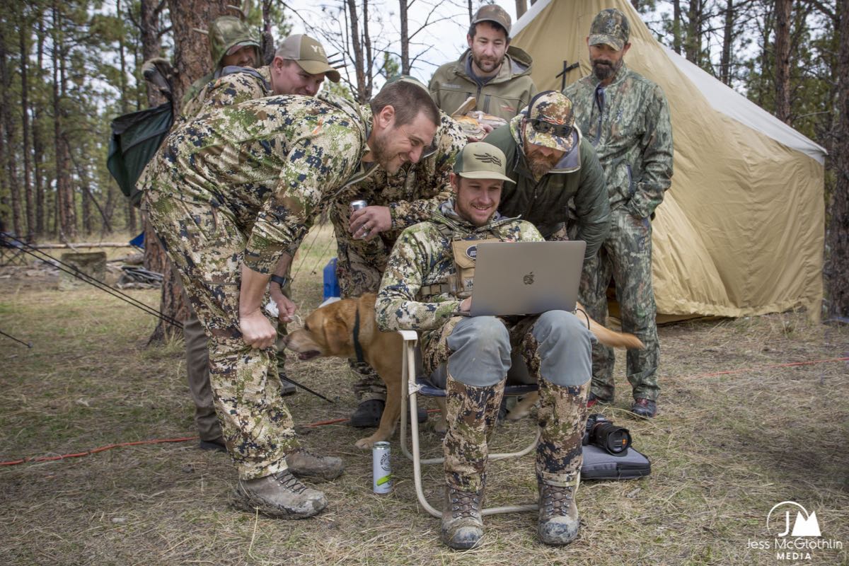 Men in camo gathered around a computer looking at footage in a wall tent camp while turkey hunting in Montana. 
