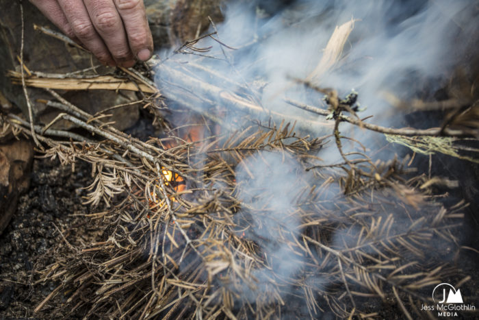 Dirty man's hand lighting fire with pine twigs and wood.