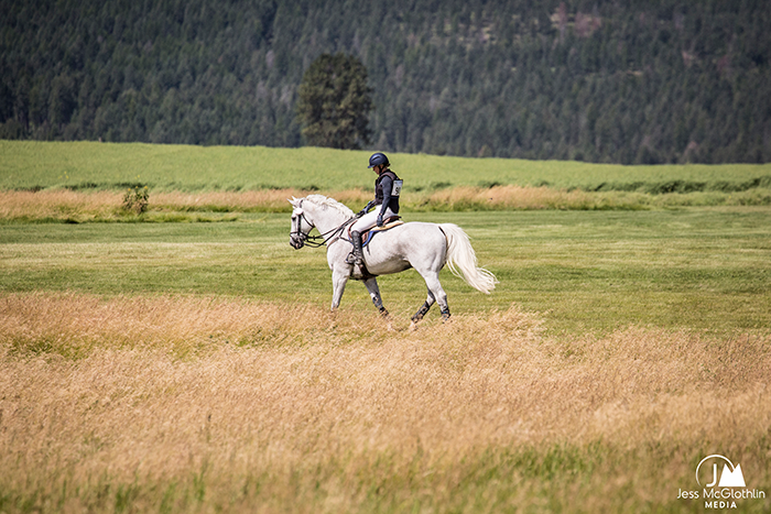 Girl riding white horse through a field in Montana at the Event at Rebecca Farm.